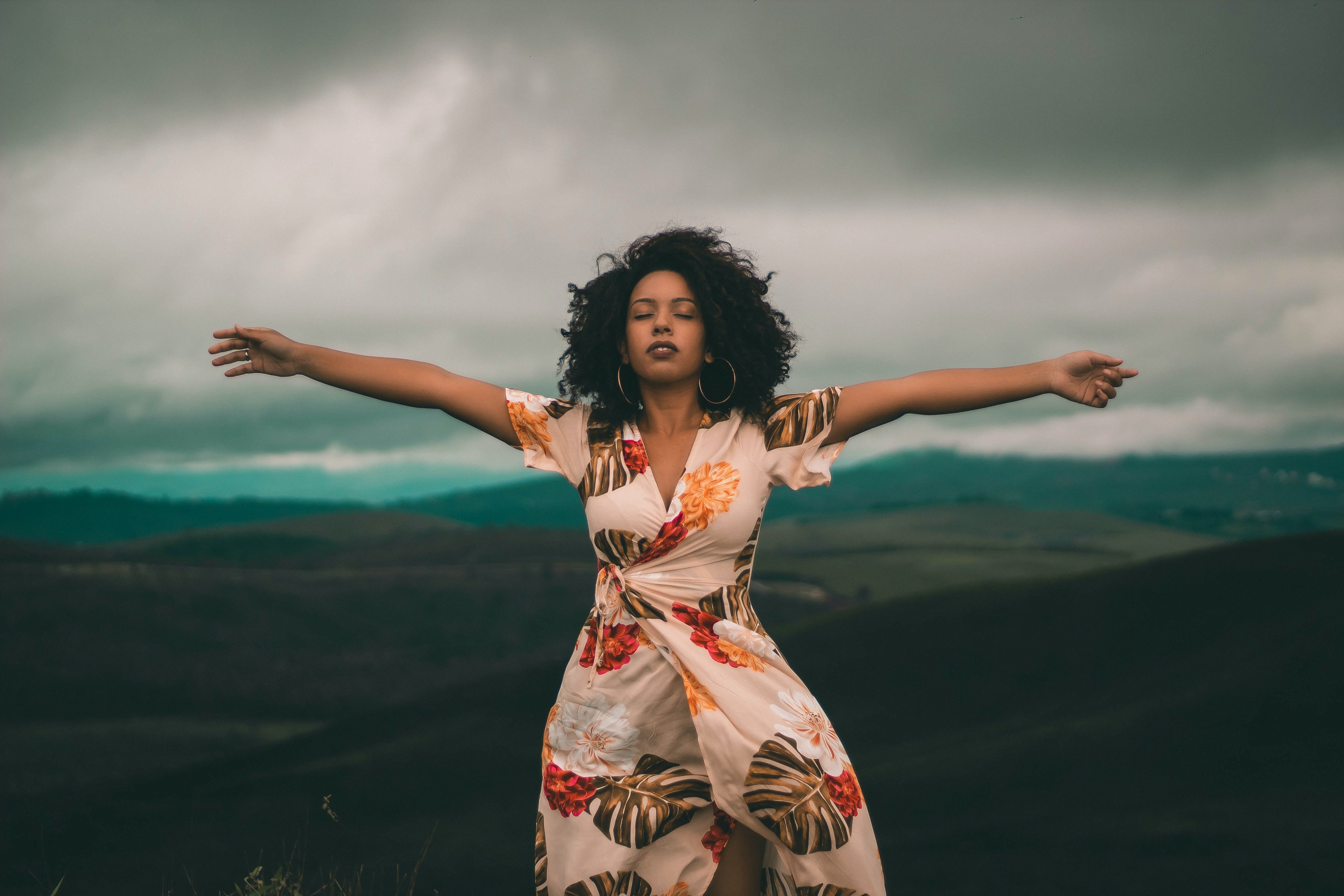 Femme en robe à fleurs les bras ouverts debout sur une colline
