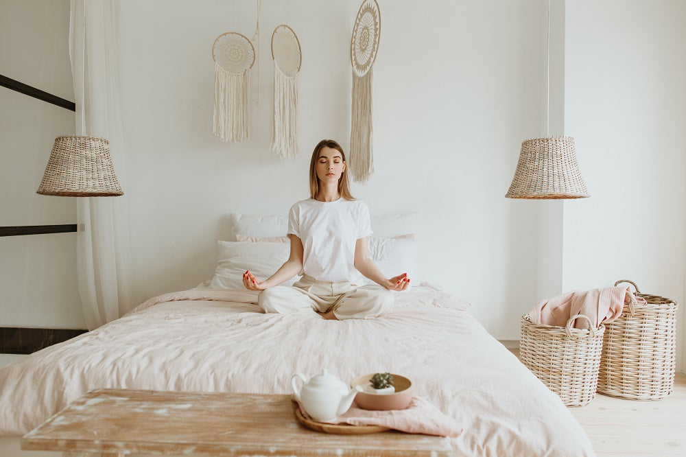 jeune femme méditant dans la posture du tailleur sur son lit